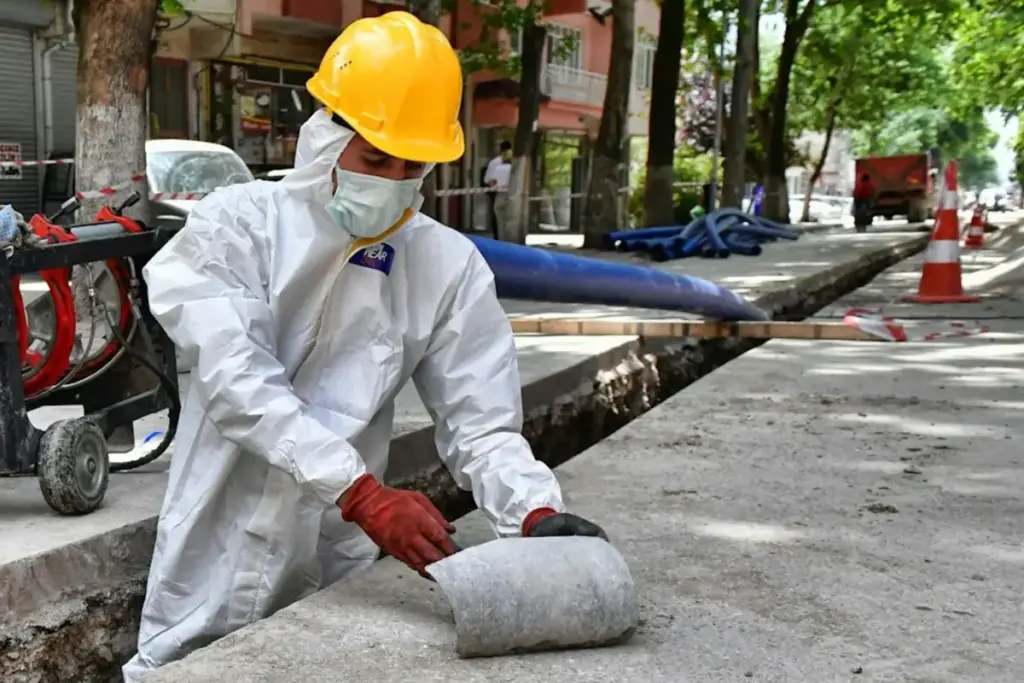 Operario con mono desechable, mascarilla y guantes sacando un tramo de tubería gris de una zanja